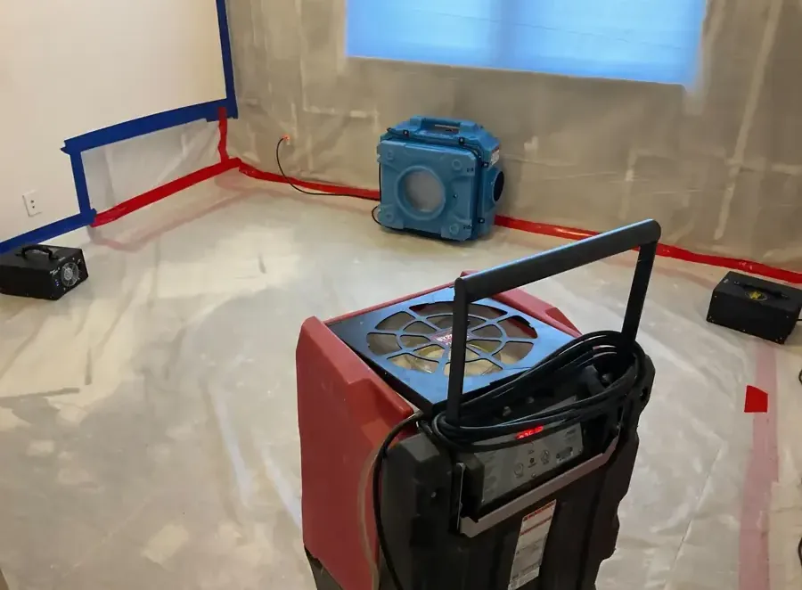 Red dehumidifier and blue air scrubber inside a room with plastic containment