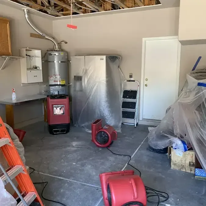 Air movers and a dehumidifier drying a garage with the ceiling opened after a water heater leak