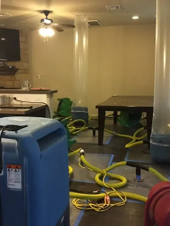 Drying machines and yellow hoses extend through an occupied interior with furniture and a ceiling fan.