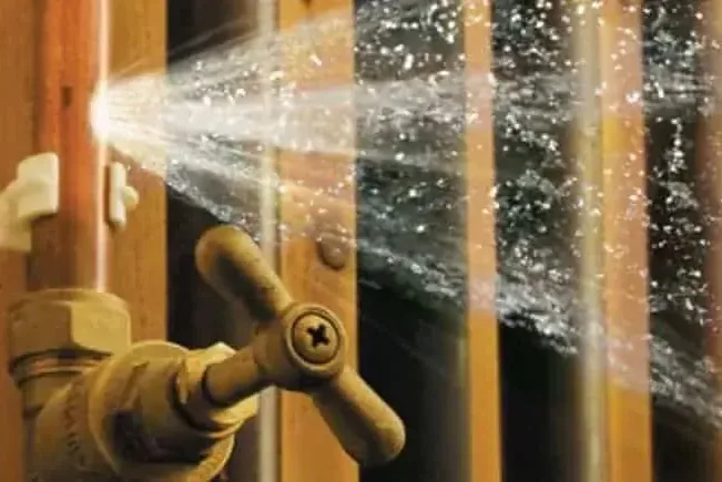 Water spraying from a burst supply pipe inside an open wall